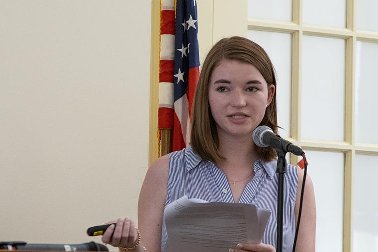 A student speaks at a lectern in front of an American flag.